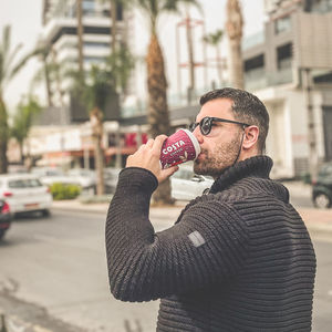 Side view of man drinking coffee in city