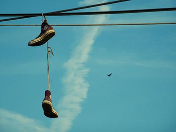 Low angle view of shoes hanging on rope against blue sky