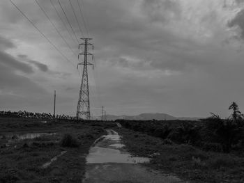 Electricity pylons against cloudy sky