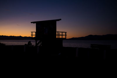 Silhouette built structure on beach against sky during sunset