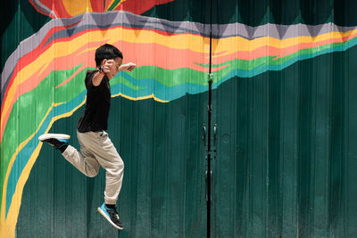 Side view of boy jumping by metallic gate