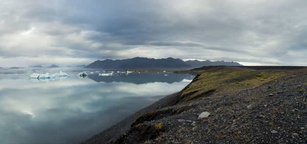 At the shore jokulsarlon of glacier lagoon lake, dramatic sky and mountains in the background