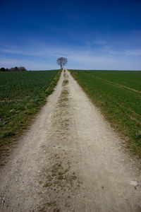 Dirt road amidst field against sky