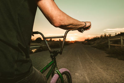 Midsection of man riding bicycle against sky during sunset