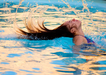 Side view of girl tossing hair in swimming pool