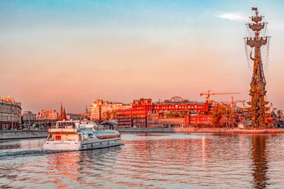 Boats in river by buildings in city against sky during sunset