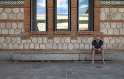 Rear view of a man sitting on brick wall