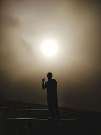 Silhouette man standing on wall against bright sun