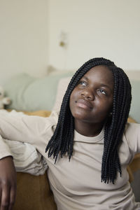 Contemplative teenage girl with braided hair sitting at home