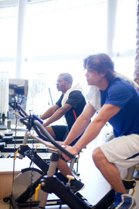 Side view of men riding exercise bikes in gym