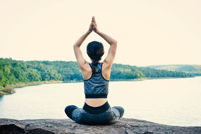 Rear view of woman practicing yoga on rock against sky