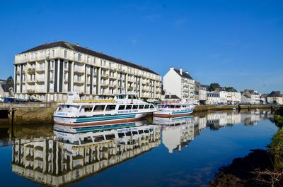 Boats moored in river by buildings against blue sky