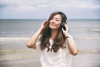 Smiling woman listening to music while standing at beach