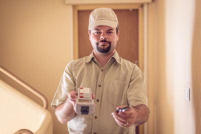 Portrait of young man holding camera at home