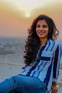 Portrait of smiling young woman standing against sky during sunset