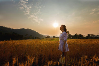 Profile view of woman standing on field against sky during sunset