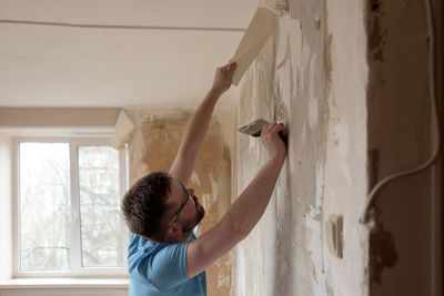 Side view of boy standing against wall at home