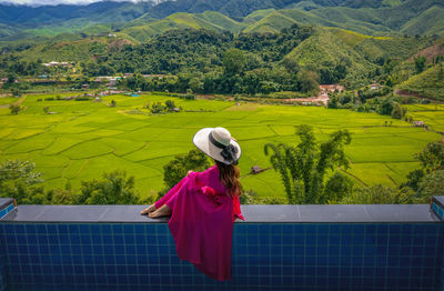 Full length of woman sitting on wall against landscape