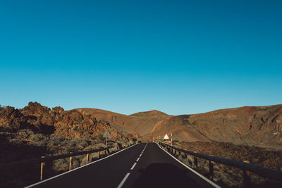 Road leading towards mountains against clear blue sky