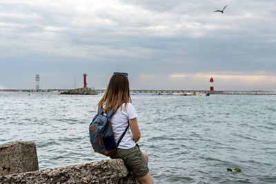 Rear view of young woman tourist looking at view of sea and cloudy sky in port, travel, landscape