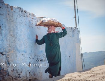 Side view of woman standing on rock against sky