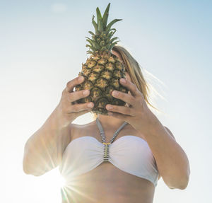 Low angle view of young woman holding pineapple against sky