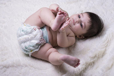 High angle view of shirtless baby girl lying on bed