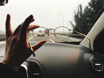 Cropped hand holding eyeglasses in front of car windshield