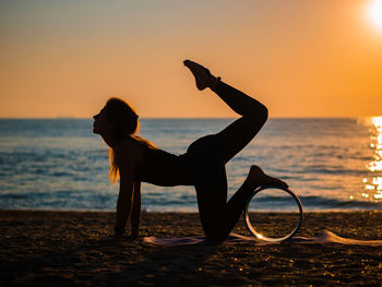 Silhouette woman doing yoga at beach against sky