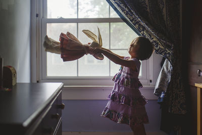 Rear view of woman standing by window at home