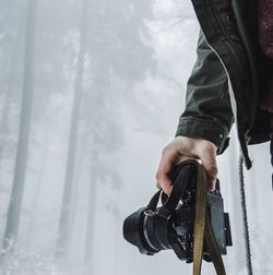 Cropped image of man holding camera at forest during foggy weather