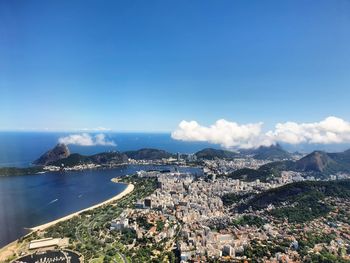 Aerial view of townscape by sea against blue sky