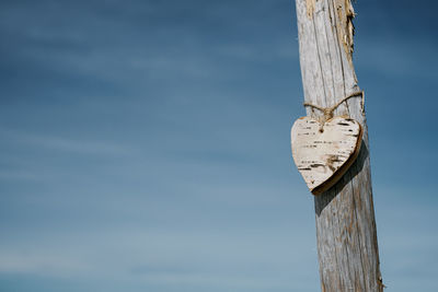 Low angle view of wooden post with hearth shaped wood against sky