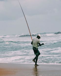 Full length of fisherman walking on shore at sea against sky