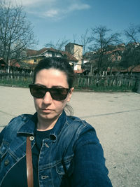 Portrait of young man wearing sunglasses standing against bare trees