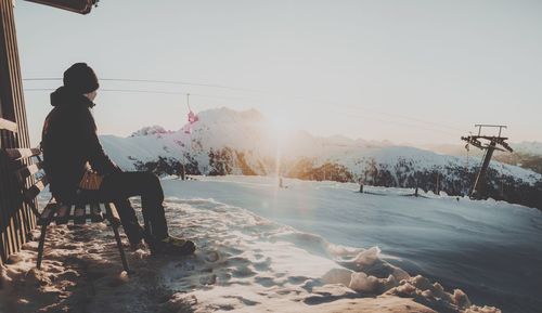 Man sitting on bench against snowcapped mountains during sunset