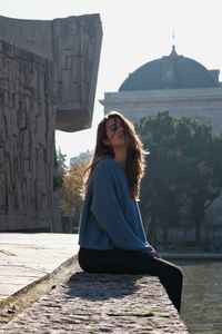 Portrait of young woman sitting against built structure