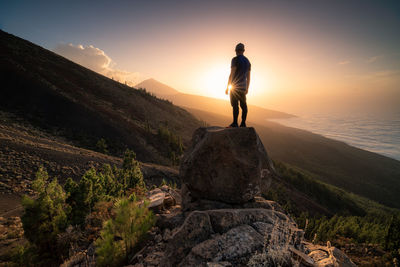 Man standing on rock against sky during sunset