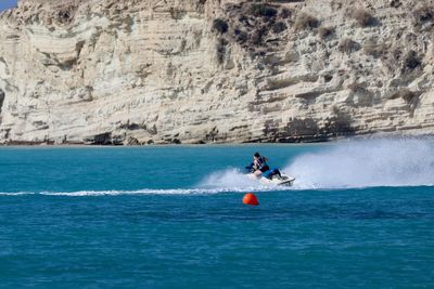 Young woman riding motorboat on sea against rock formation sky during sunny day