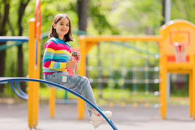 Cute smiling little girl, 5-6 years old, sitting with a plastic bottle of water on the playground