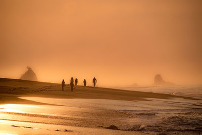 Silhouette people at beach against sky during sunset