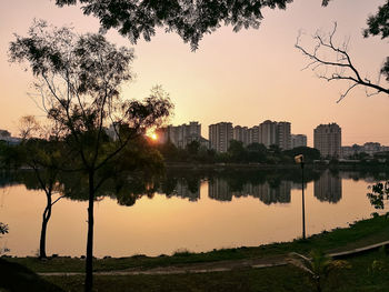 Scenic view of lake by buildings against sky during sunset