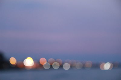 Defocused image of illuminated lights in sea against sky