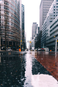 Wet city street by modern buildings against sky during monsoon