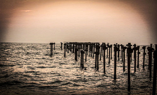 Wooden posts in sea against sky at sunset