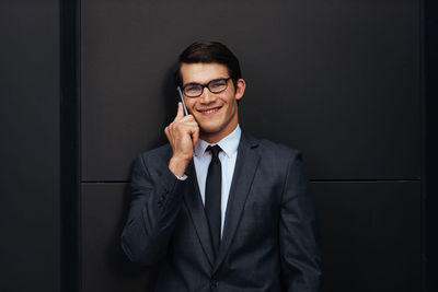 Portrait of smiling young man standing against black background