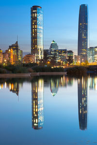 Illuminated buildings by river against sky at dusk