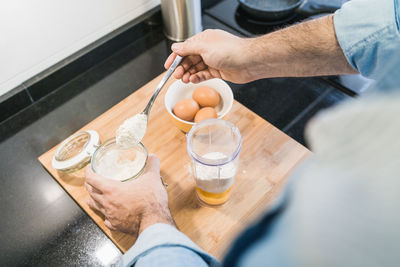 Man cooking in the kitchen in a denim shirt. an anonymous man is holding a spoon of flour