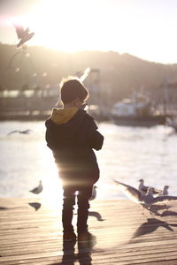 Boy standing on pier over lake against sky during sunset