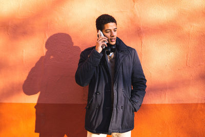 Young man using smart phone while standing against wall